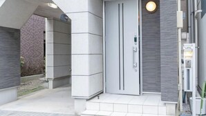 A modern building entrance with a grey door, a small outdoor area, and a light fixture above the door. - 10 Min Walk to Ikebukuro Station 4BR Private House 3 Min to Kanamecho Sleeps 8 (Tokyo)