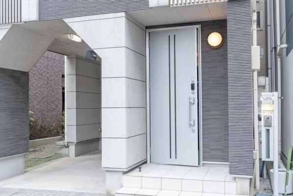 A modern building entrance with a grey door, a small outdoor area, and a light fixture above the door. - 10 Min Walk to Ikebukuro Station 4BR Private House 3 Min to Kanamecho Sleeps 8 (Tokyo)