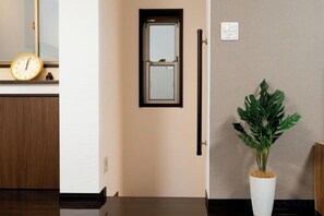 A hallway with a wooden floor, a white door, a wall-mounted clock, and a potted plant. - 10 Min Walk to Ikebukuro Station 4BR Private House 3 Min to Kanamecho Sleeps 8 (Tokyo)