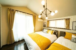 A hotel room with two beds, a chandelier, a large window with curtains, and a brick wall. - Kanamecho Modern House (Tokyo)