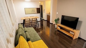 A modern living room with a sectional sofa, a flat-screen TV, and a dining area with chairs and a table. - 10 Min Walk to Ikebukuro Station 4BR Private House 3 Min to Kanamecho Sleeps 8 (Tokyo)