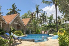 A pool area with lounge chairs, a swimming pool, and palm trees. - Coconut Village Guest House Lembongan RedPartner (Bali)