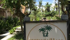 A sign for Coconut Village Guest House with palm trees and a stone pathway. - Coconut Village Guest House Lembongan RedPartner (Bali)