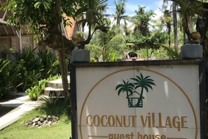 A sign for Coconut Village Guest House with palm trees and a stone pathway. - Coconut Village Guest House Lembongan RedPartner (Bali)