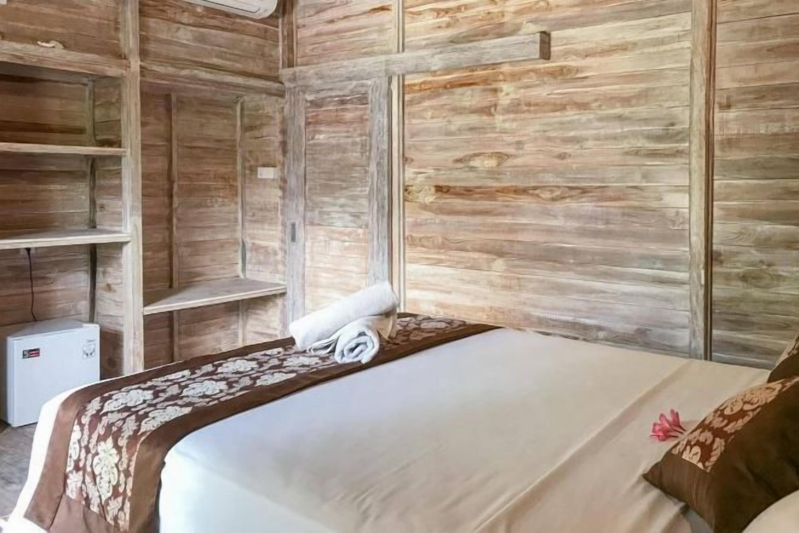 A room with a bed, a small white appliance, and wooden paneling.
