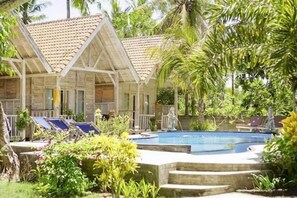A pool area with lounge chairs, a small pool, and wooden structures with tiled roofs. - Coconut Village Guest House Lembongan RedPartner (Bali)