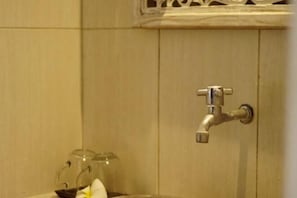 A bathroom with a single faucet mounted on the wall, a glass container with a flower, and a decorative wooden panel above the faucet. - Coconut Village Guest House Lembongan RedPartner (Bali)