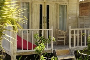 A wooden cabin with a porch, a red cushion, and a staircase leading to the entrance.