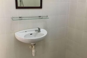 Un baño con un lavamanos blanco, un estante de vidrio encima y un espejo en la pared.