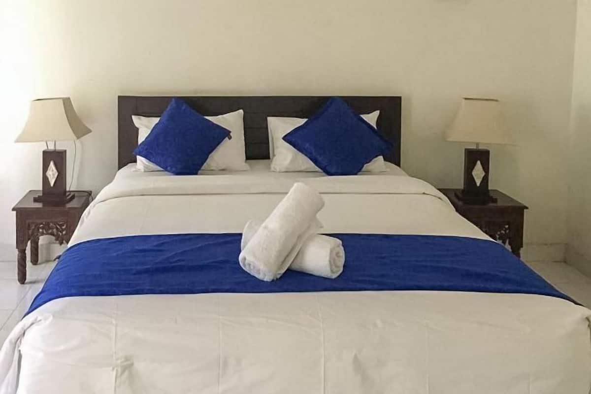 A neatly made bed with a blue and white bedspread, two nightstands with lamps, and a wooden headboard.