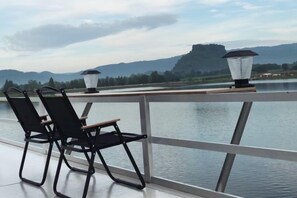 A balcony with two chairs and two floor lamps overlooking a body of water and hills. - Grandmaaoi House (Phu Pha Man)