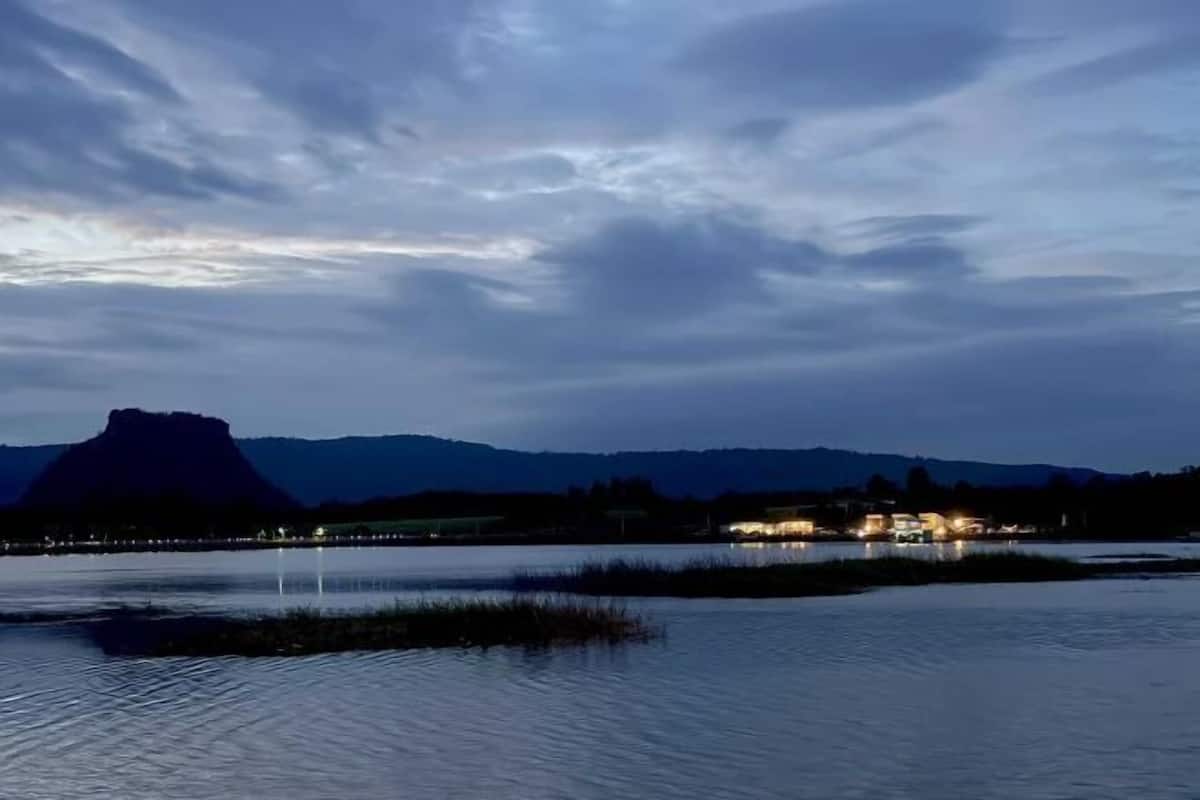 A lakeside view with a mountain in the background and a building with lights on the shore.