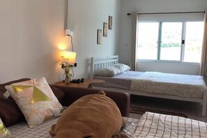 A bedroom with a bed, a bedside table with a lamp, a window, and a couch. - Grandmaaoi House (Phu Pha Man)