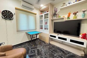 A living room with a dartboard, a pool table, a TV, and shelves with decorative items.