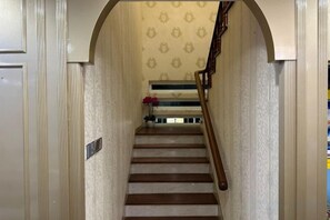 A staircase with a wooden handrail, a patterned wall, and a small vase with flowers at the top. - Melodies Castle Homestay (Johor Bahru)