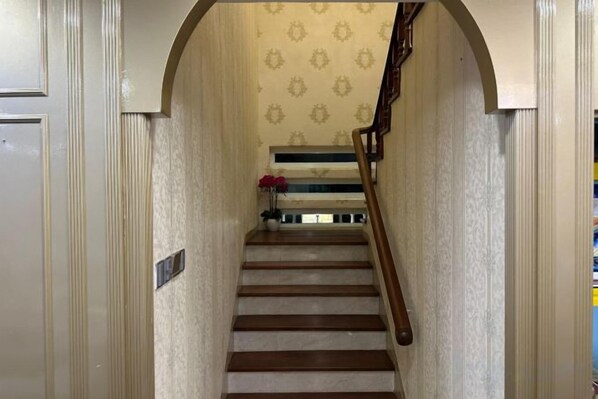 A staircase with a wooden handrail, a patterned wall, and a small vase with flowers at the top. - Melodies Castle Homestay (Johor Bahru)