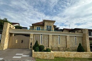 A large, modern house with a gated entrance, stone facade, and a well-maintained lawn.