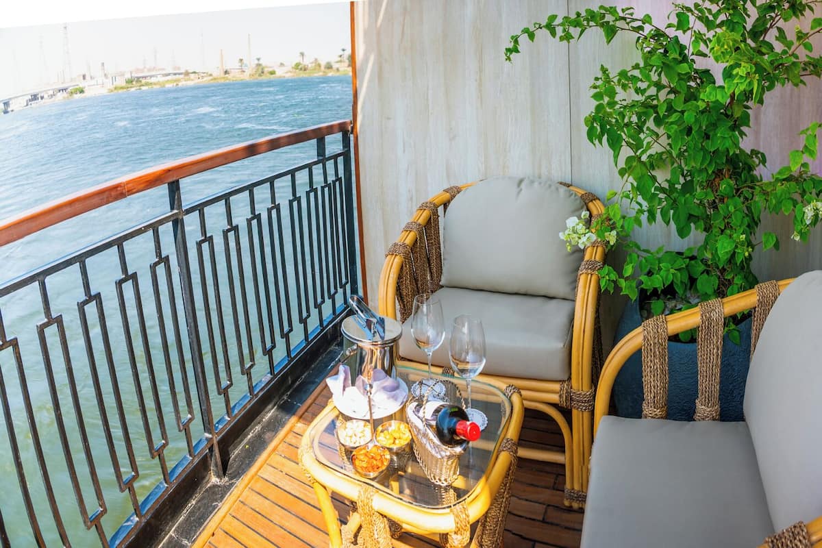 A balcony with wicker chairs, a table with drinks, and a view of the water.