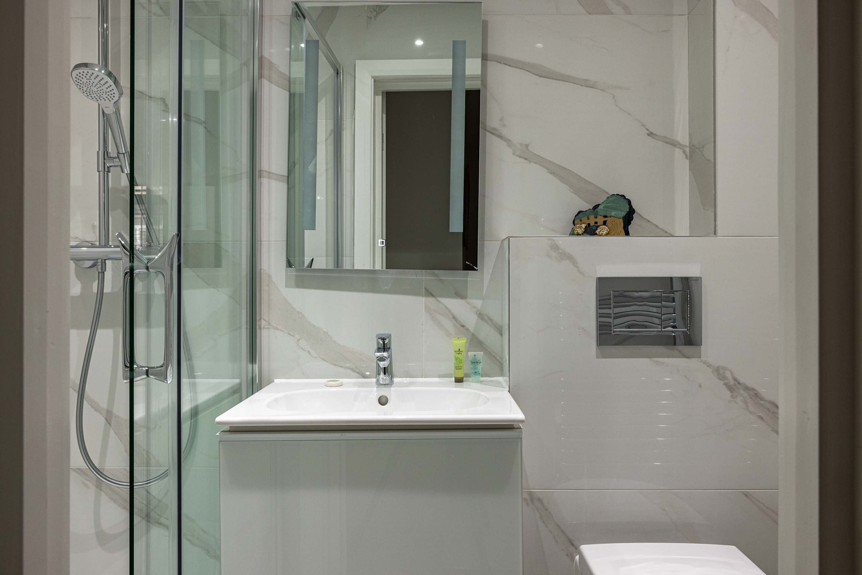 A modern bathroom with a glass shower enclosure, a white sink, and a marble-tiled wall.