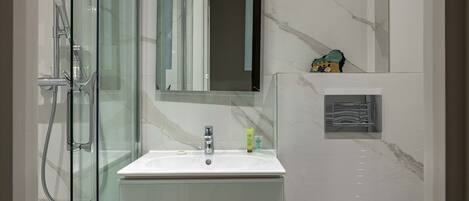 A modern bathroom with a glass shower enclosure, a white sink, and a marble-tiled wall.