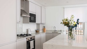 A modern kitchen with white cabinetry, a built-in microwave, a gas stove, and a large island with a vase of flowers.