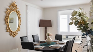 A dining area with a marble table, black chairs, a vase with flowers, and a gold-framed mirror on the wall.