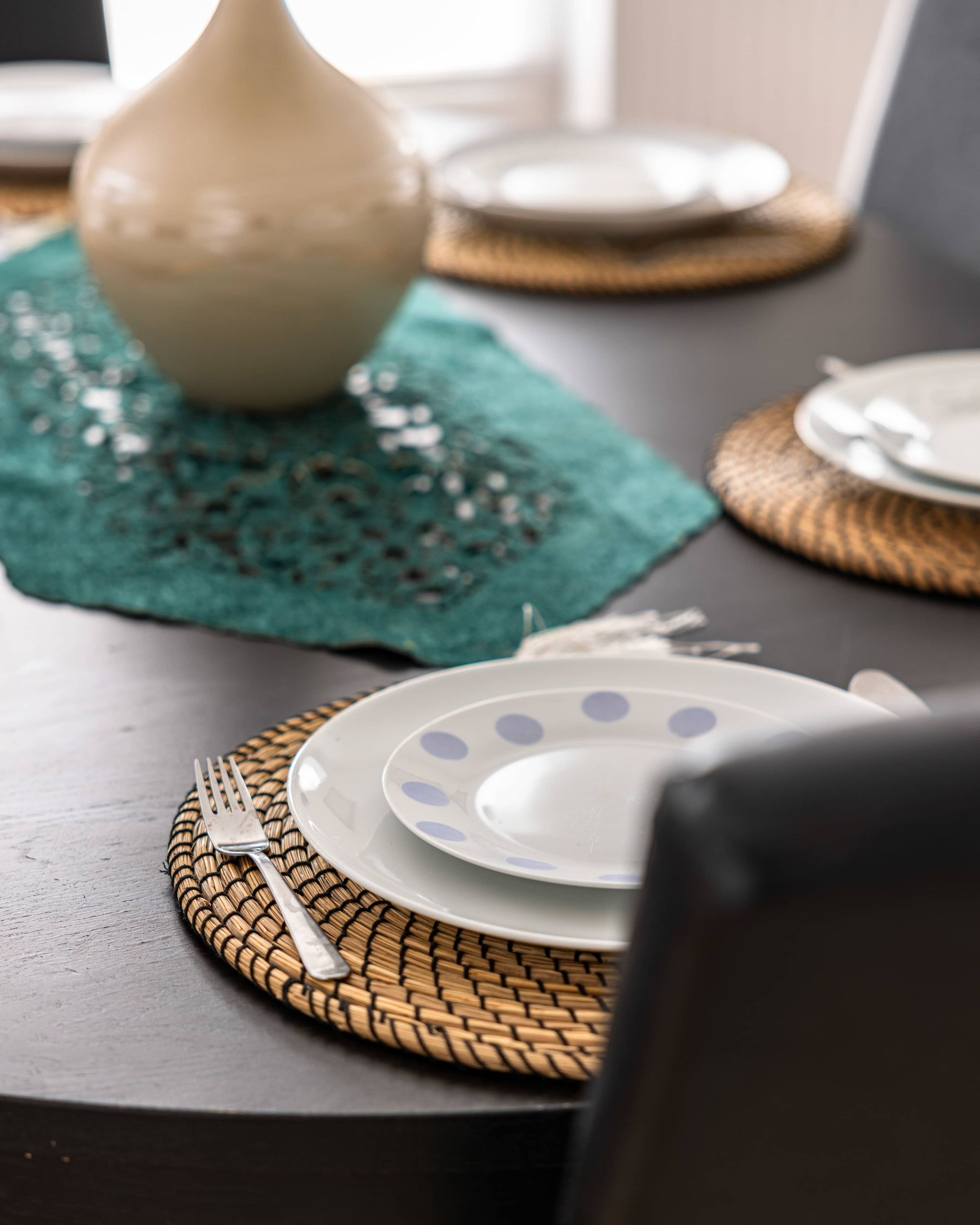 Una mesa de comedor con un posavasos tejido, un plato blanco con lunares azules y un tenedor plateado.
