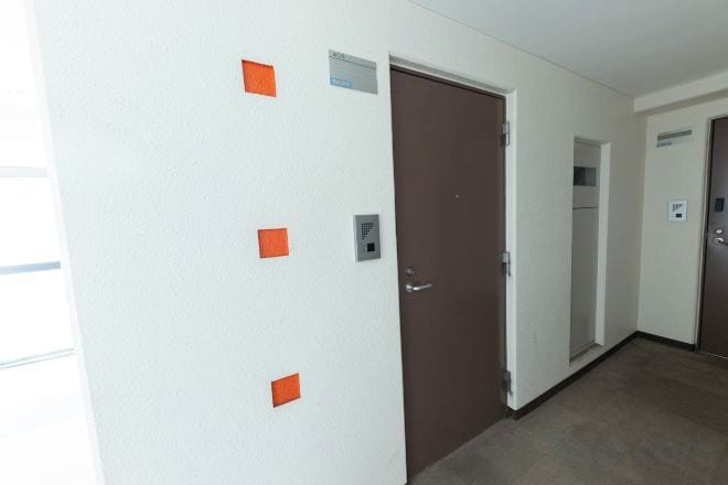 A hallway with a brown door, a white wall with orange markings, and a carpeted floor.