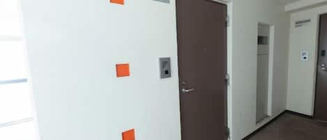 A hallway with a brown door, a white wall with orange markings, and a carpeted floor.
