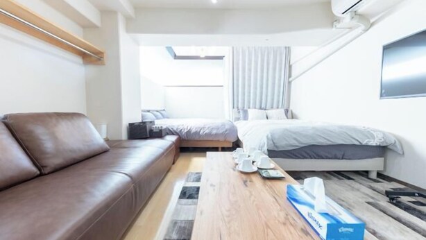 A modern hotel room with a brown leather sofa, a wooden coffee table, a bed with grey bedding, and a large window with curtains. - 2 stops to Shinjuku, 7 minutes to train station, for families and couples, close to Tokyo City Hall (Tokyo)