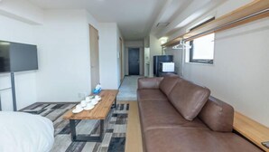 A modern hotel room with a sofa, a wooden table with shoes, a TV, and a corridor leading to a bathroom. - 2 stops to Shinjuku, 7 minutes to train station, for families and couples, close to Tokyo City Hall (Tokyo)