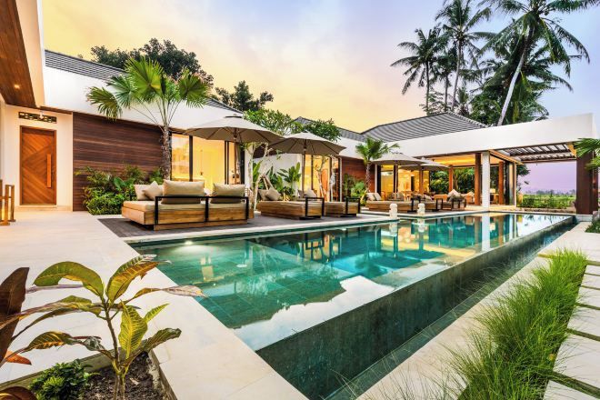 A modern pool area with lounge chairs and umbrellas, surrounded by tropical plants and palm trees.