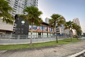 A modern building with a large mural, palm trees, and a fenced area. - CONEZION BY FEEL HOME (Serdang)