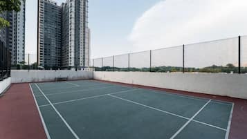 An outdoor tennis court with a white fence and buildings in the background.