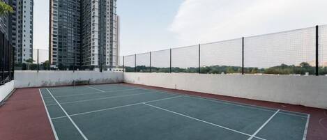 An outdoor tennis court with a white fence and buildings in the background.