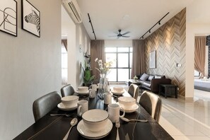 A dining area with a table set for four, chairs, a vase with flowers, and a sofa in the background. - CONEZION BY FEEL HOME (Serdang)