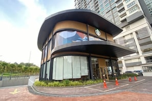 A modern building with a curved facade, large windows, and a visible Starbucks sign. - CONEZION BY FEEL HOME (Serdang)