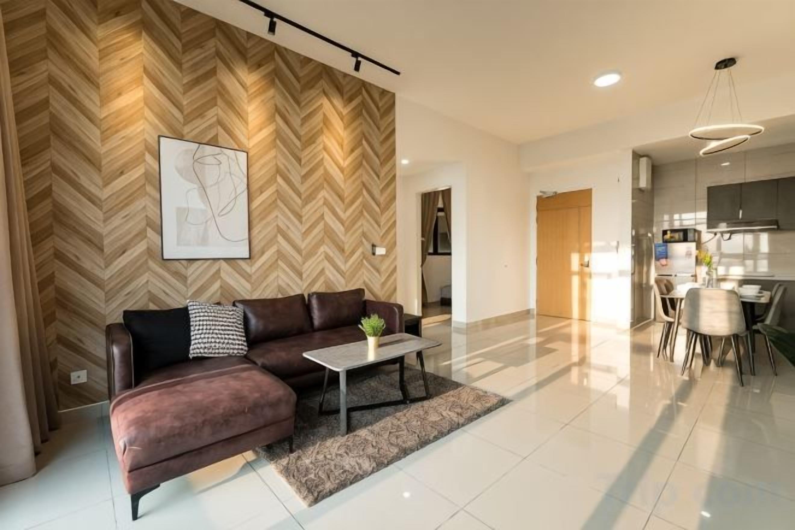 A modern living room with a herringbone-patterned wall, a sectional sofa, a coffee table, and a dining area with a chandelier.