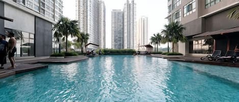 A swimming pool surrounded by high-rise buildings, with lounge chairs and palm trees.