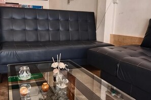 A modern living room with a dark leather sofa, a glass coffee table with decorative items, and a white wall. - Annie Backpacker Hostel (Vientiane)