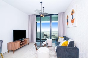 A modern living room with a flat-screen TV, a sofa set, a coffee table, and a large window offering a city view. - bnbme Address Beach Apt, Near Bluewaters & JBR (Dubai)