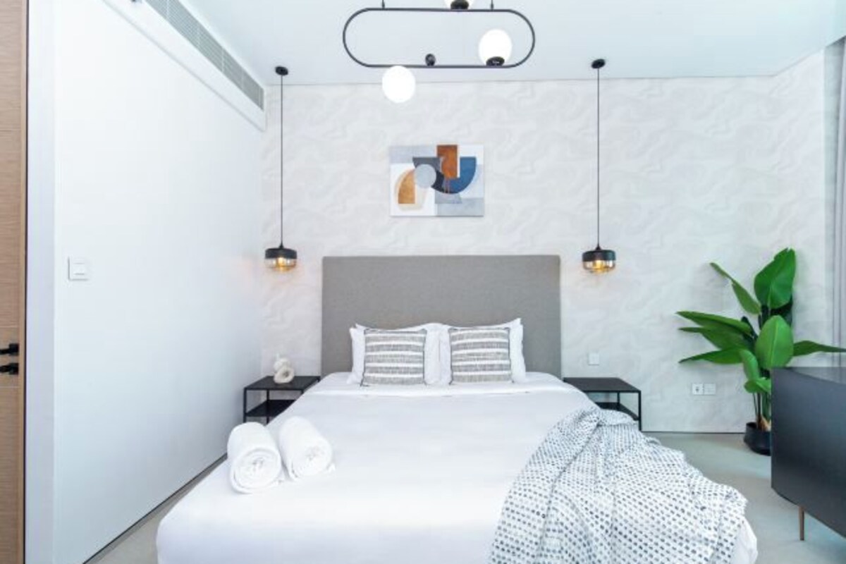 A modern bedroom with a large bed, bedside tables, a ceiling light fixture, and a wall-mounted artwork.