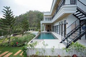A modern two-story building with a swimming pool, surrounded by lush greenery and a hilly landscape. - Tierra en Sierra (Pak Chong)