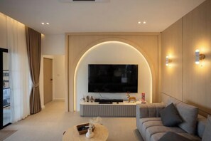 A modern living room with a large flat-screen TV mounted on a wooden wall, a sofa, and a coffee table. - Tierra en Sierra (Pak Chong)
