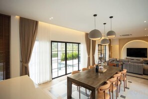 A modern dining area with a large table and chairs, a sofa, and a television in the background. - Tierra en Sierra (Pak Chong)