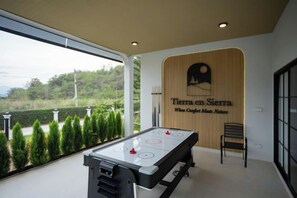 A room with a foosball table, a wooden wall with the text 'Tierra en Sierra,' and a view of greenery outside. - Tierra en Sierra (Pak Chong)