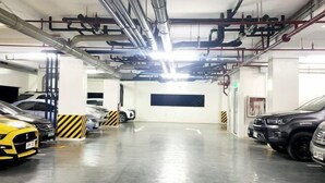 Een parkeergarage met meerdere geparkeerde auto's, zichtbare leidingen en ventilatiekanalen aan het plafond, en een schone, goed verlichte omgeving.