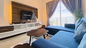 Ein modernes Wohnzimmer mit Flachbildfernseher, einer Couch, einem Couchtisch und einem großen Fenster mit Vorhängen.