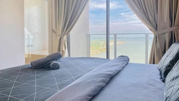 Een slaapkamer met een bed, gordijnen en uitzicht op zee.
