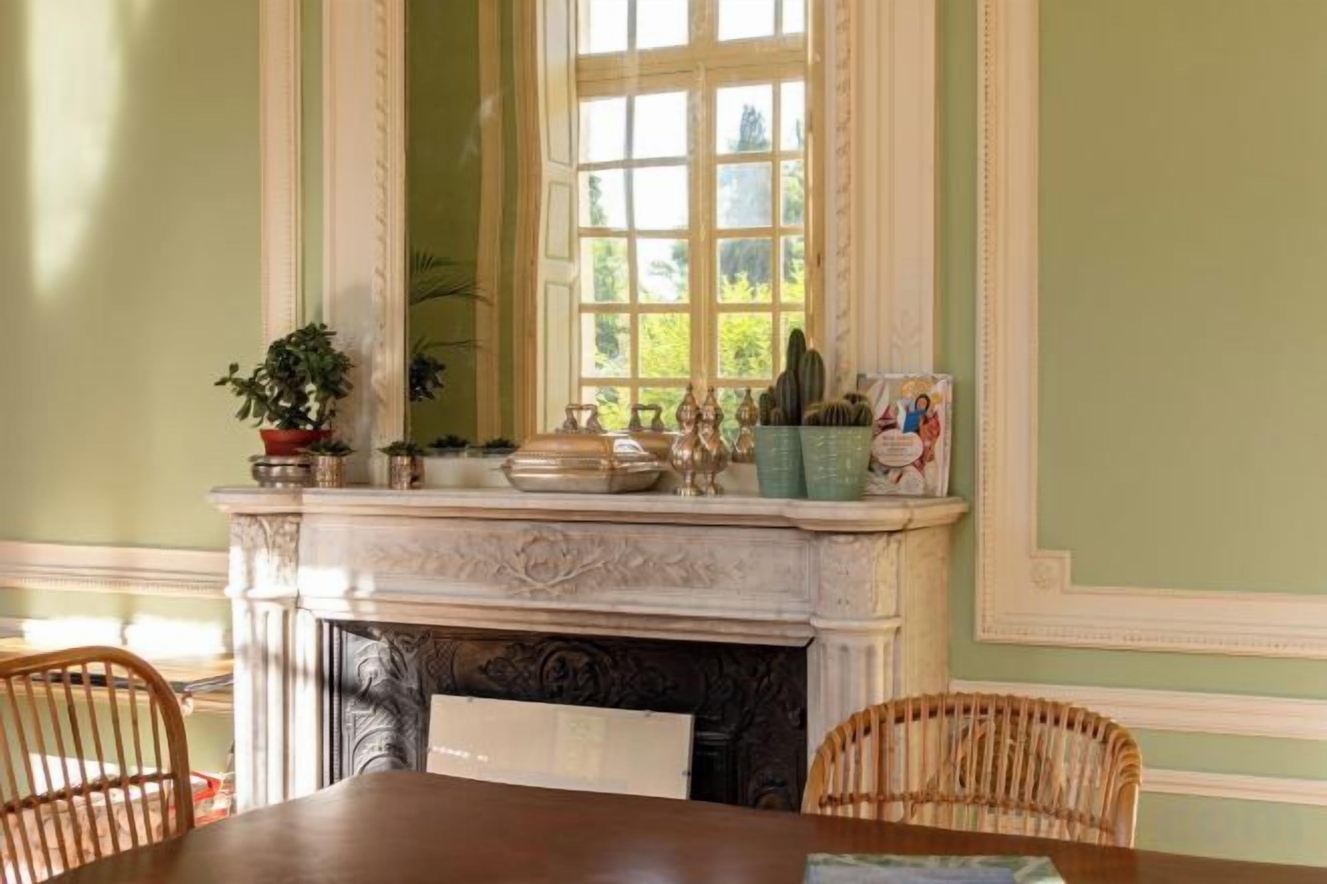 A dining area with a fireplace, a table, chairs, and a window with a view of greenery.